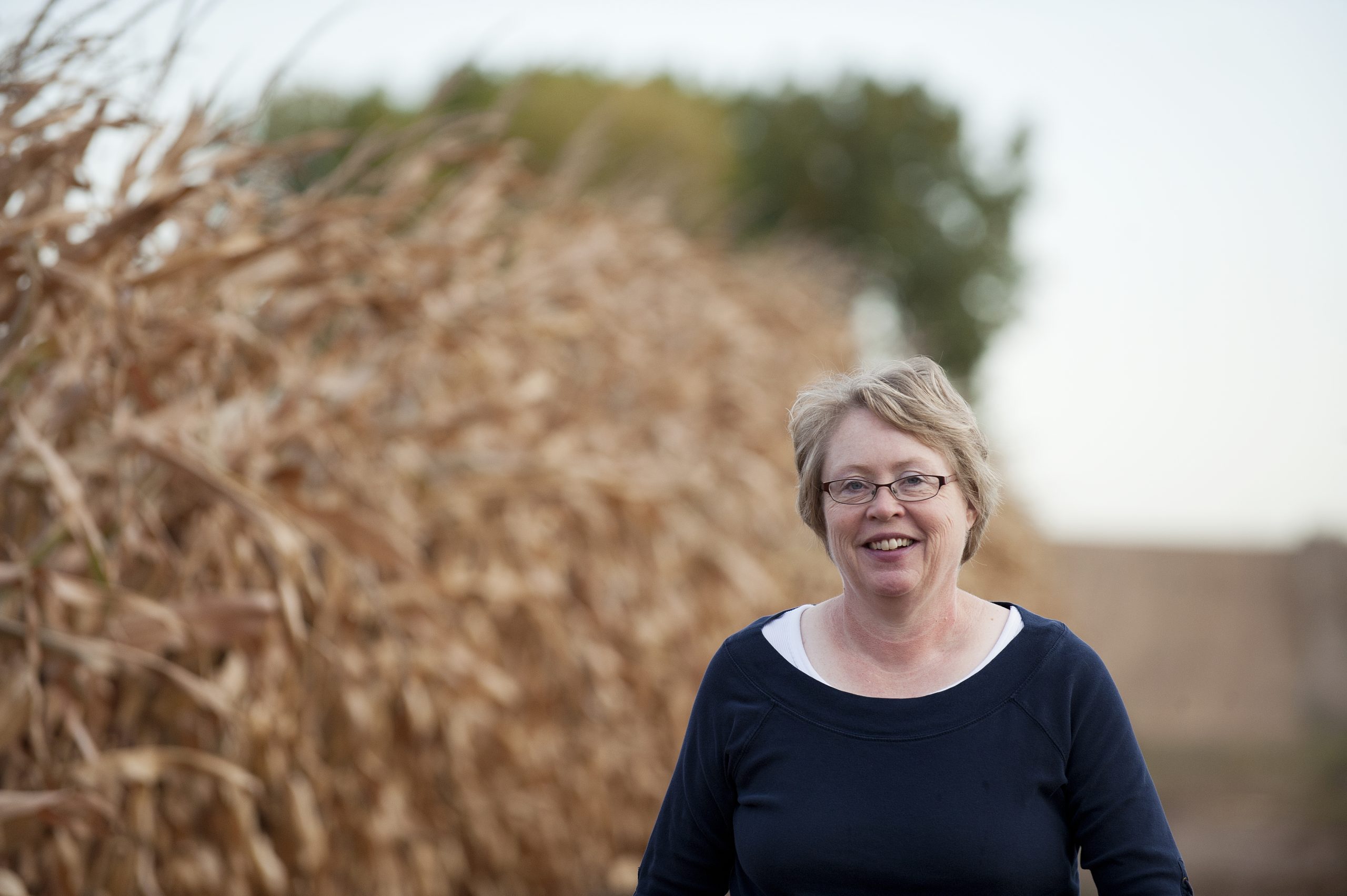 A woman stands in front of a corn field ready for harvest