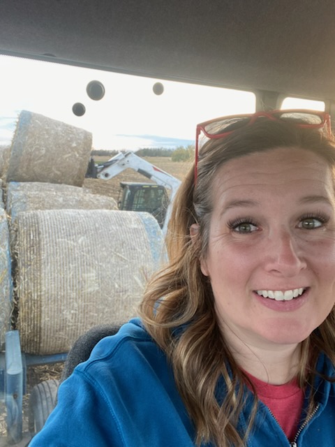 Woman takes a selfie with round bales in the background.