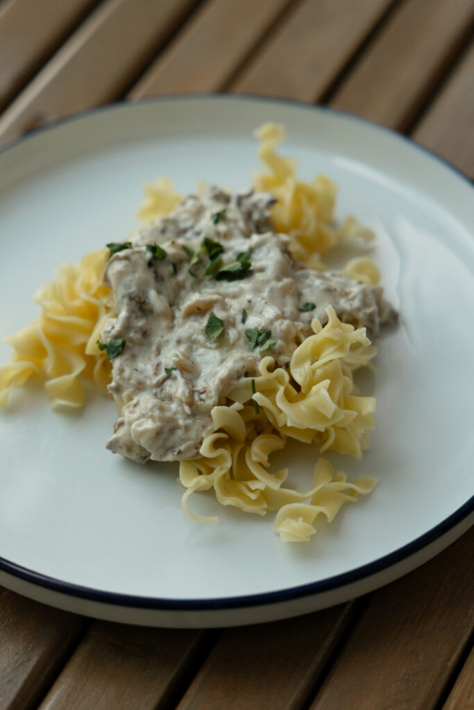 A white plate with egg noodles and beef stroganoff.