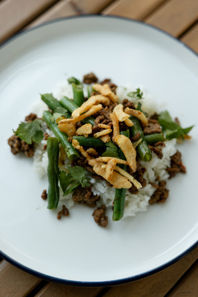 Rice, beef, green beans, and fried onions on a white plate